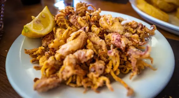 Plato de puntillas de calamar fritas, crujientes y doradas, servido con una rodaja de limón.