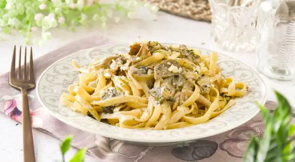 Pasta con setas cremosa, servida en un plato decorado, con un tenedor de bronce al lado.