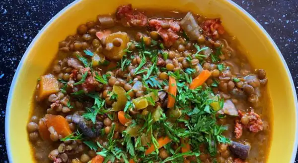 Un reconfortante potaje de lentejas con trozos de chorizo, zanahoria y perejil fresco, servido en un cuenco amarillo.