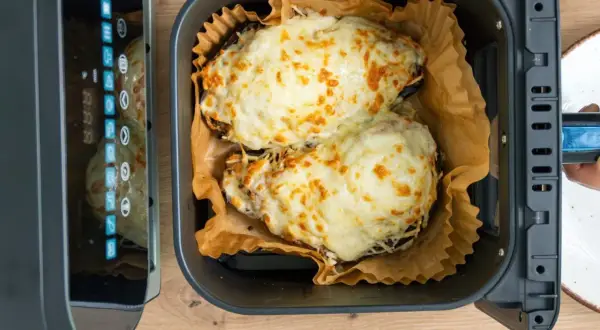 Dos berenjenas rellenas, cubiertas de queso derretido y dorado, listas para disfrutar tras su paso por la freidora de aire.