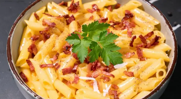 Un tazón de macarrones a la carbonara, cubiertos con trozos de tocino crujiente, perejil fresco y pimienta negra.