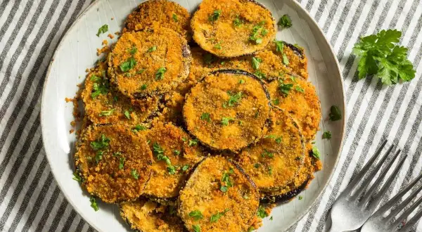 Berenjenas rebozadas con harina y huevo, doradas y crujientes, espolvoreadas con perejil fresco. Un plato delicioso y fácil de preparar.