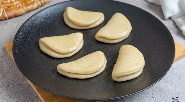 Cinco panes bao crudos en un plato negro, listos para la receta.