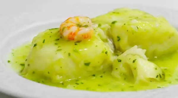 Merluza en salsa verde, un plato tradicional con trozos de pescado blanco y un camarón encima, bañado en una deliciosa salsa verde.