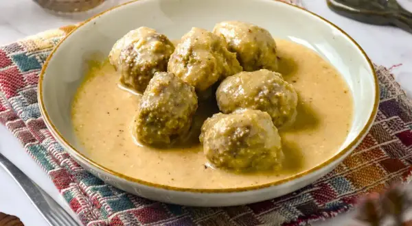 Deliciosas albóndigas en salsa de almendras, servidas en un plato sobre un mantel colorido.