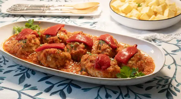 Sabrosos **rollos de bonito** en salsa de tomate, coronados con pimientos rojos. Acompañados de patatas fritas en un bol.