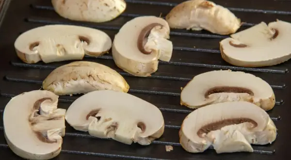 Champiñones cortados a la mitad y enteros sobre una parrilla, listos para deliciosas recetas con champiñones.