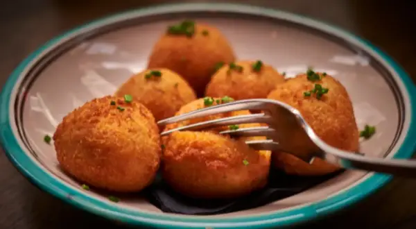 Croquetas de puchero doradas y crujientes, servidas en un plato con un tenedor listo para probarlas.