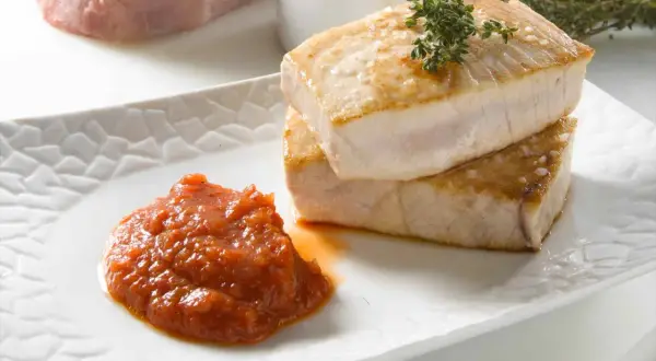 Dos jugosos trozos de atún a la plancha, con sal gruesa y una ramita de tomillo, acompañados de una porción de salsa de tomate casera.