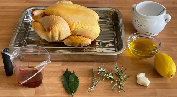 Un pollo crudo listo para asar, con ingredientes como limón, aceite, hierbas, ajo y sal. ¡Perfecto para un delicioso pollo al ast!