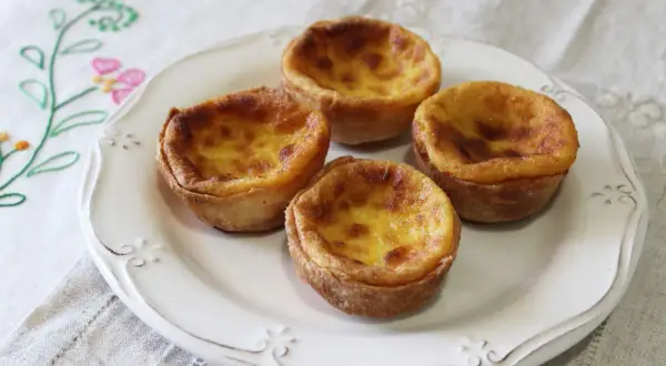 Cuatro deliciosos pastelitos de arroz con relleno cremoso y dorado, servidos en un plato blanco sobre un mantel bordado.