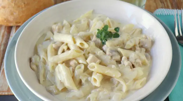 Un plato cremoso de macarrones con nata y trocitos de pollo, decorado con una ramita de tomillo.