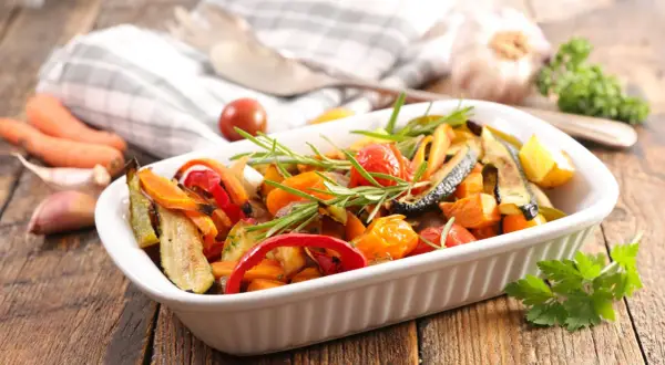 Deliciosas verduras al horno, como calabacín, pimientos y tomates cherry, con romero fresco, listas para servir.