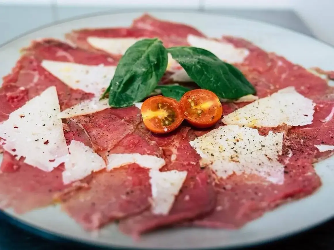 Carpaccio de ternera con queso parmesano, hojas de albahaca y tomates cherry cortados por la mitad.