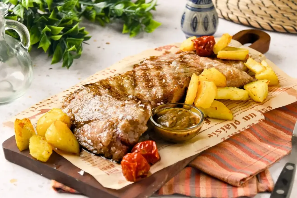 Jugosa carne al ajillo, servida con patatas rústicas y salsa, sobre papel de periódico. ¡Un festín para los sentidos!