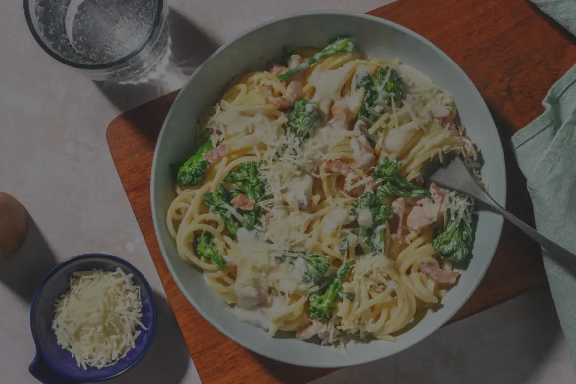 Un plato de pasta carbonara con huevo, brócoli y queso rallado, listo para disfrutar.