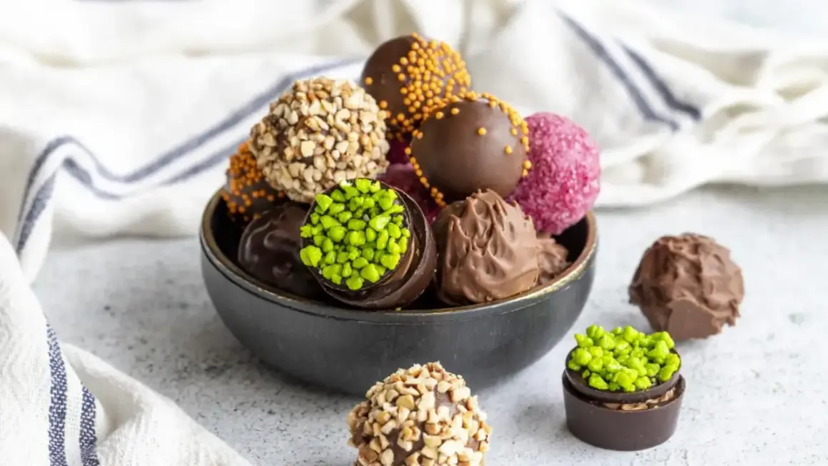 Un tazón lleno de deliciosas trufas de chocolate, algunas cubiertas de frutos secos, otras con chispas de colores y pistachos.