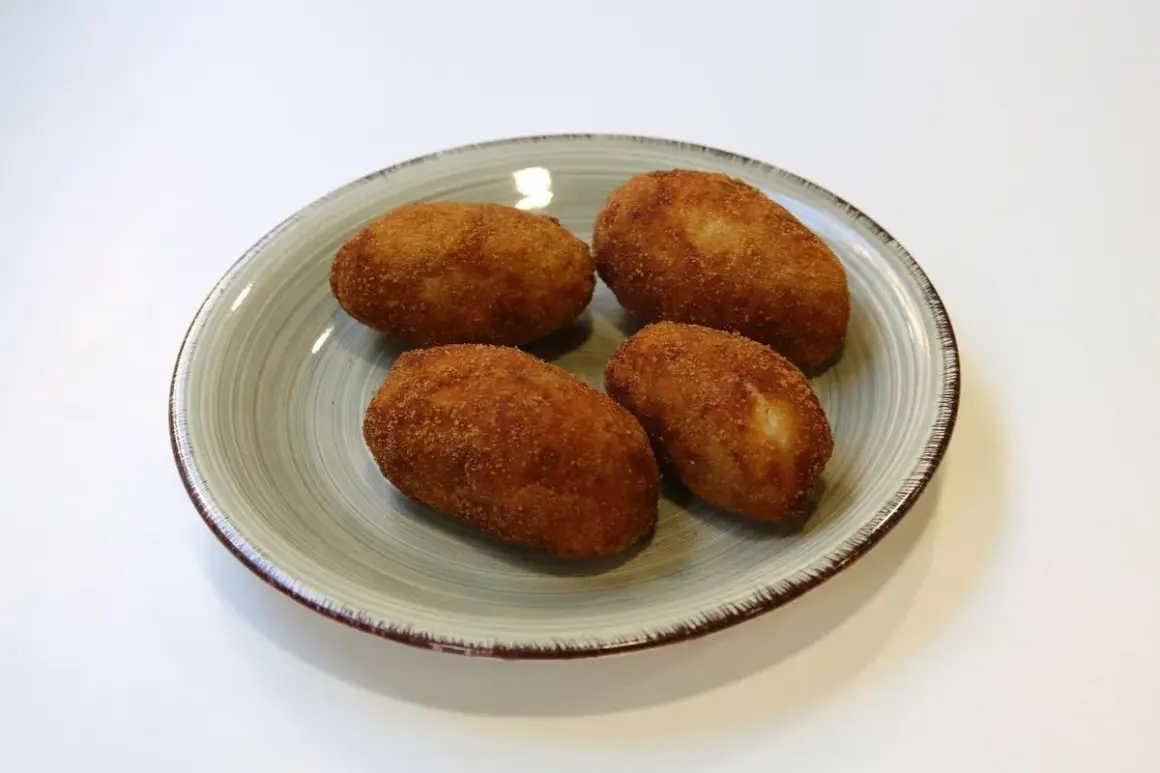 Cuatro croquetas de pollo de la abuela doradas y crujientes en un plato.