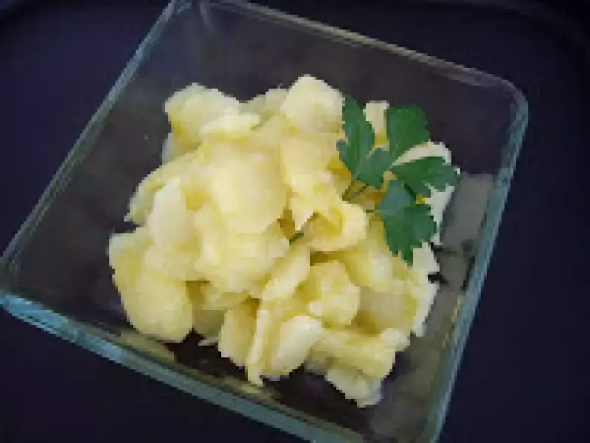 Un cuenco de cristal contiene patatas al montón, un plato sencillo y reconfortante, adornado con una ramita de perejil fresco.
