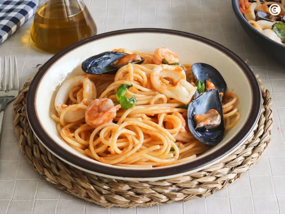 Un plato de espaguetis a la marinera con gambas, calamares y mejillones, servido en un cuenco sobre una esterilla de mimbre.