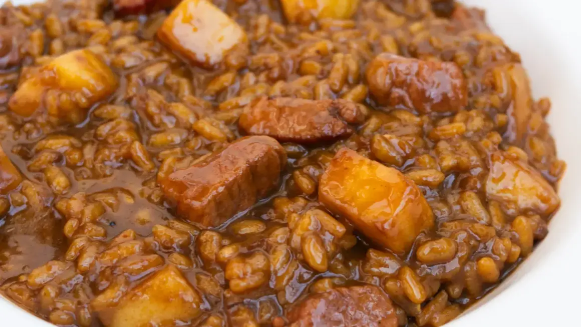 Un plato de arroz con acelgas y trozos de carne en una salsa oscura y apetitosa.