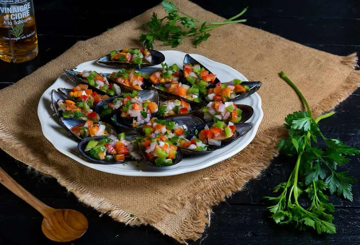 Mejillones a la vinagreta, frescos y coloridos, servidos en una concha con picadillo de verduras.