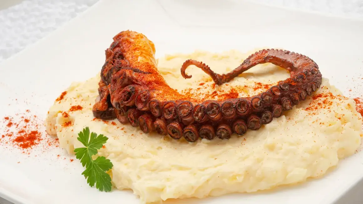 Un tentáculo de pulpo a la plancha, crujiente y especiado, reposa sobre un puré cremoso.