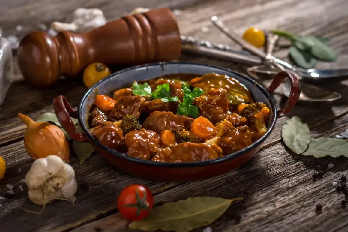 Caldereta de cordero humeante, con trozos de carne tierna, zanahoria y brócoli, servida en una cazuela rústica.