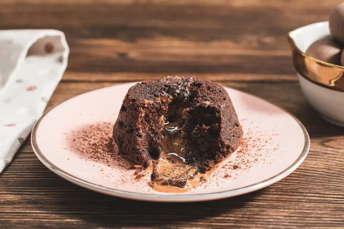 Coulant de chocolate con centro líquido y cremoso, espolvoreado con cacao en polvo sobre un plato rosa.