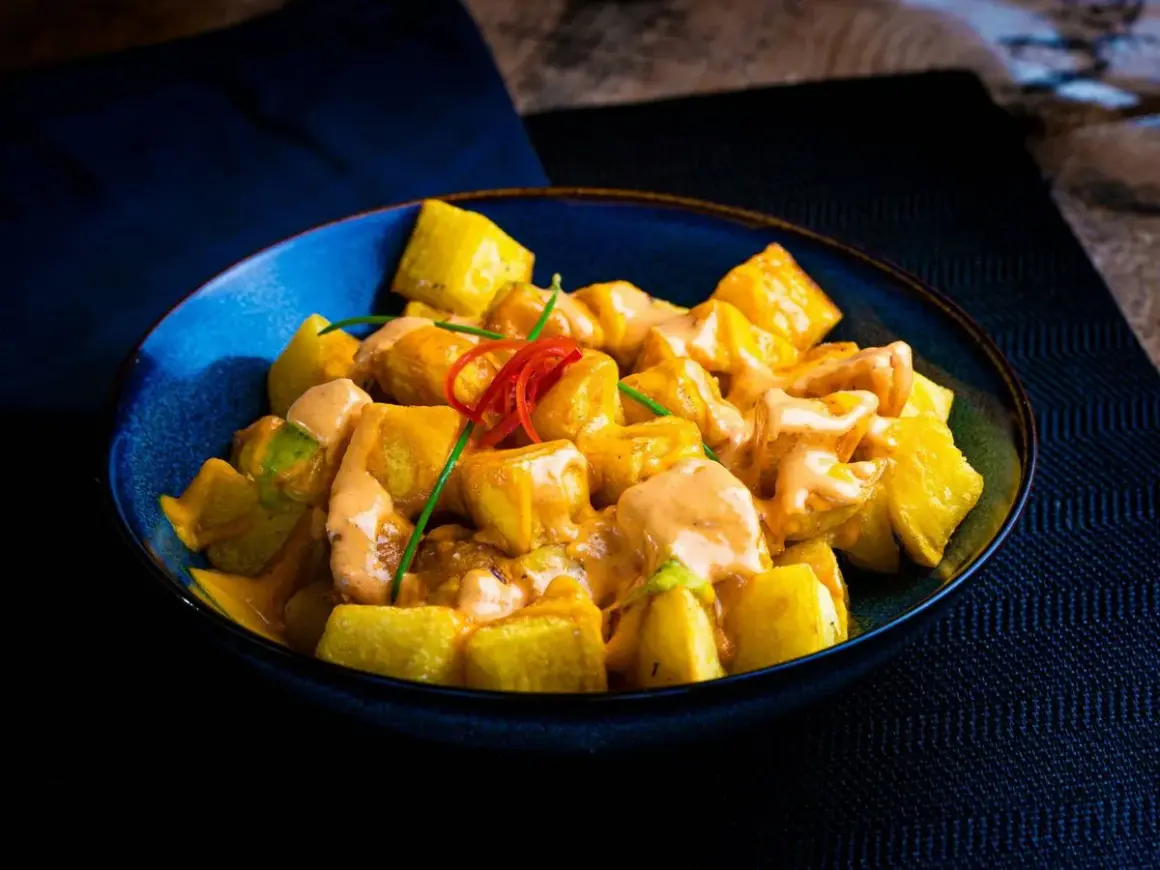 Patatas bravas receta: trozos dorados de patata cubiertos con una cremosa salsa rosada y decorados con pimiento rojo y cebollino.
