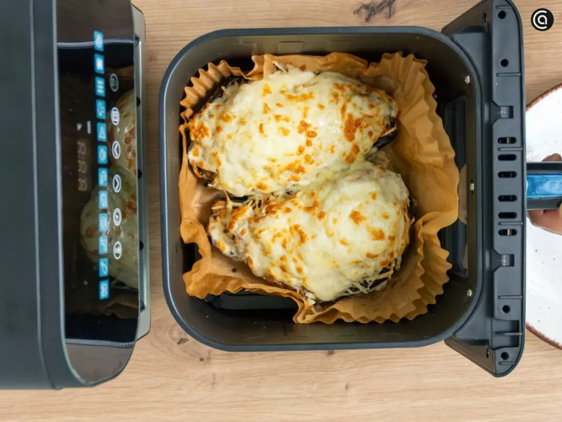 Dos berenjenas rellenas, cubiertas de queso derretido y dorado, listas para disfrutar tras su paso por la freidora de aire.