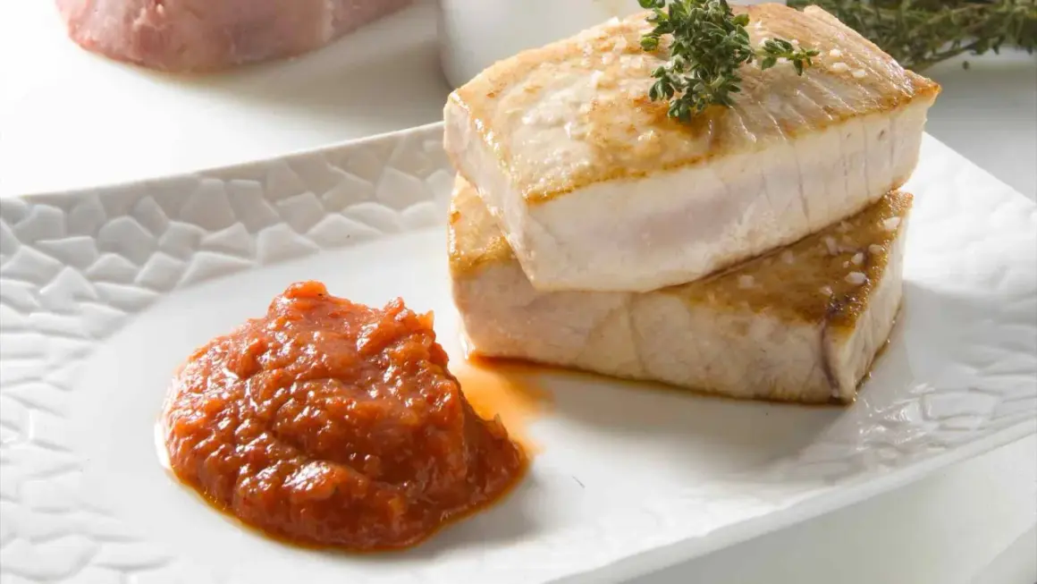 Dos jugosos trozos de atún a la plancha, con sal gruesa y una ramita de tomillo, acompañados de una porción de salsa de tomate casera.