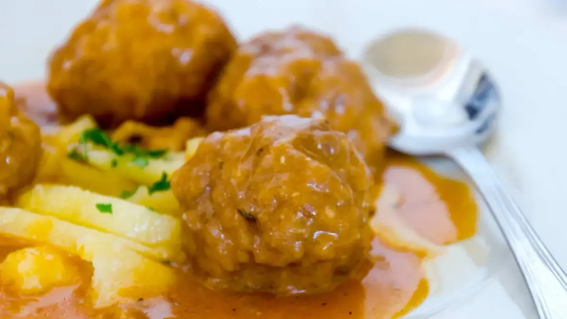 Albondigas a la jardinera, jugosas y cubiertas de salsa, acompañadas de patatas y perejil. Un plato casero listo para disfrutar.