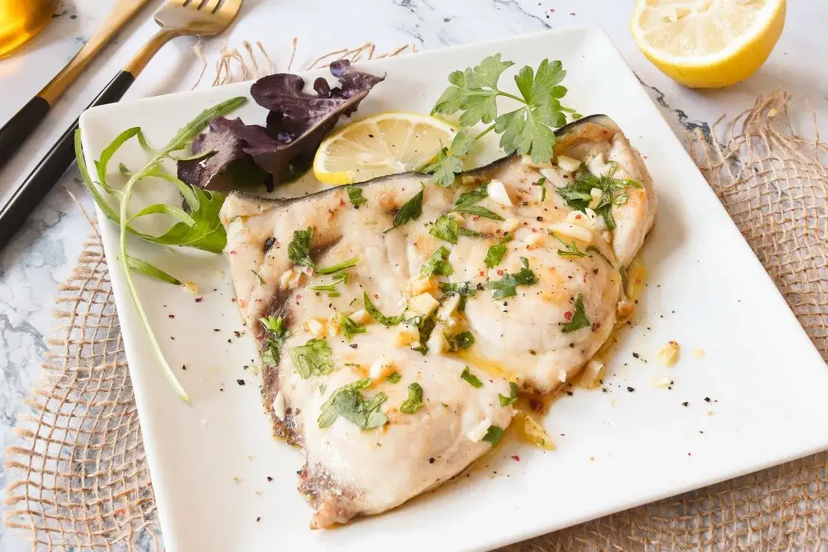 Un jugoso emperador a la plancha, bañado en aceite de oliva y ajo, con perejil fresco y una rodaja de limón. Servido con hojas verdes.