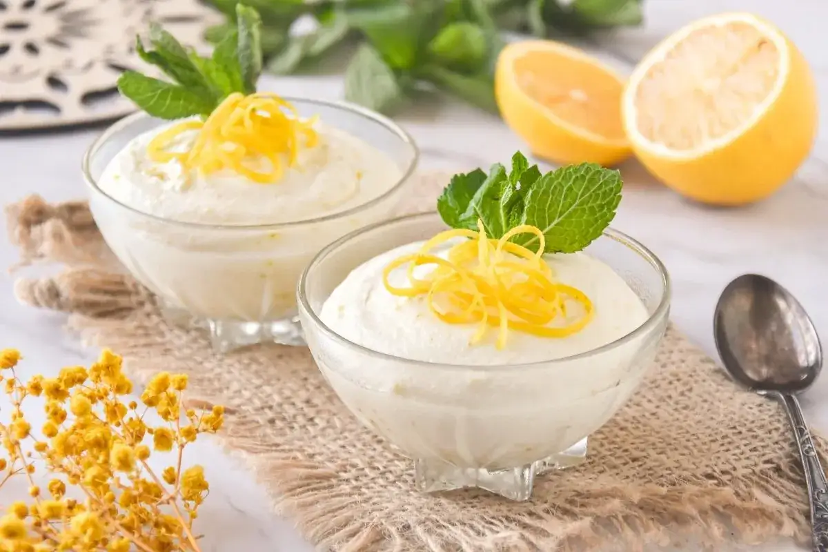 Dos copas de cremoso helado de lim&oacute;n, decoradas con ralladura y menta fresca. Limones cortados al fondo.