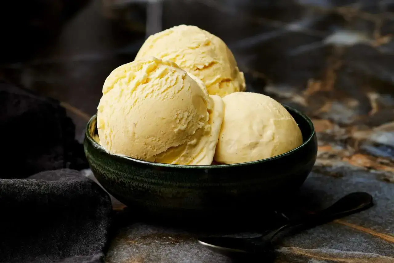Tres bolas de helado cremoso de vainilla en un cuenco verde oscuro. Perfecto para aprender como hacer helado casero.