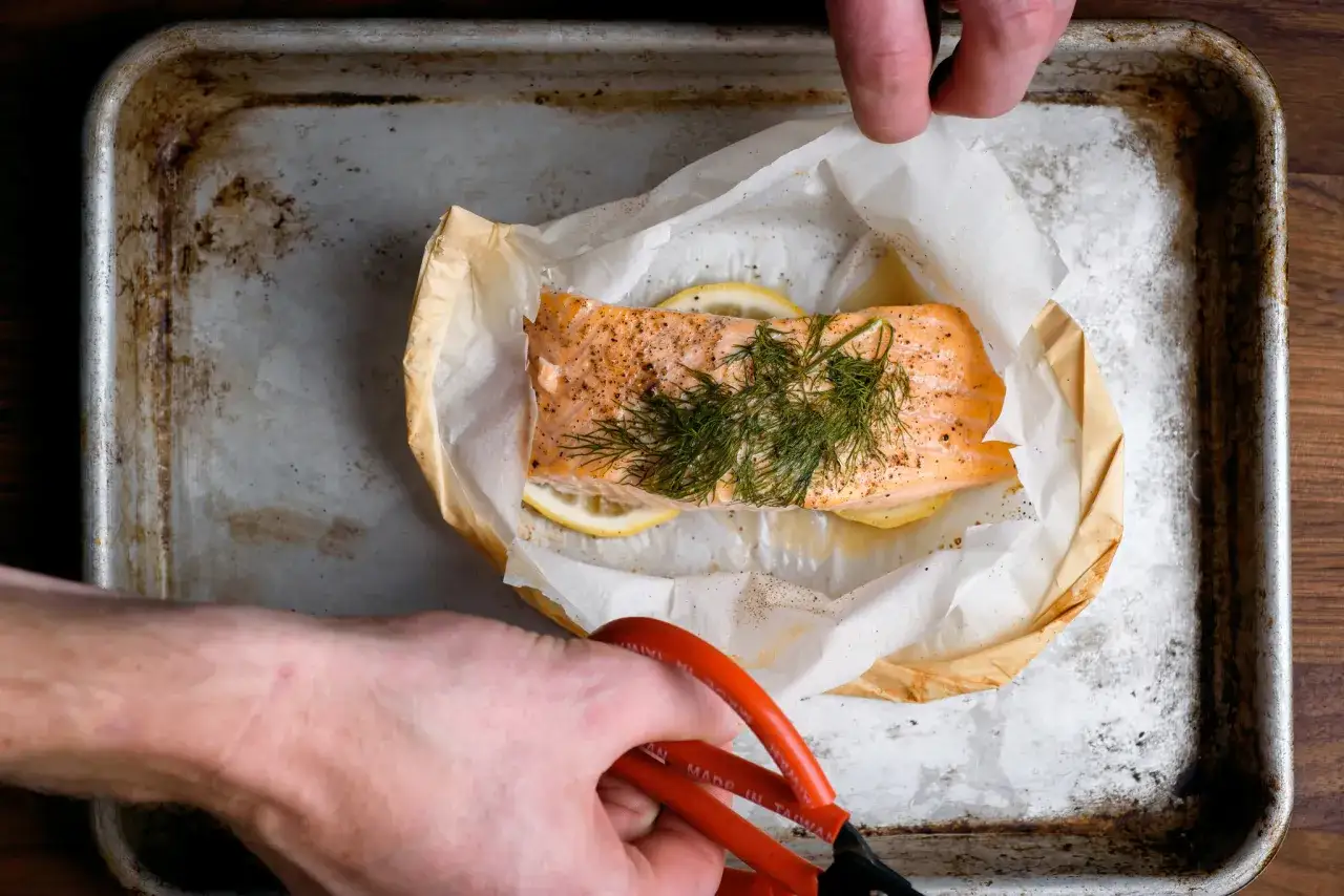 Un trozo de salm&oacute;n al papillote con lim&oacute;n y eneldo, listo para hornear en una bandeja met&aacute;lica.