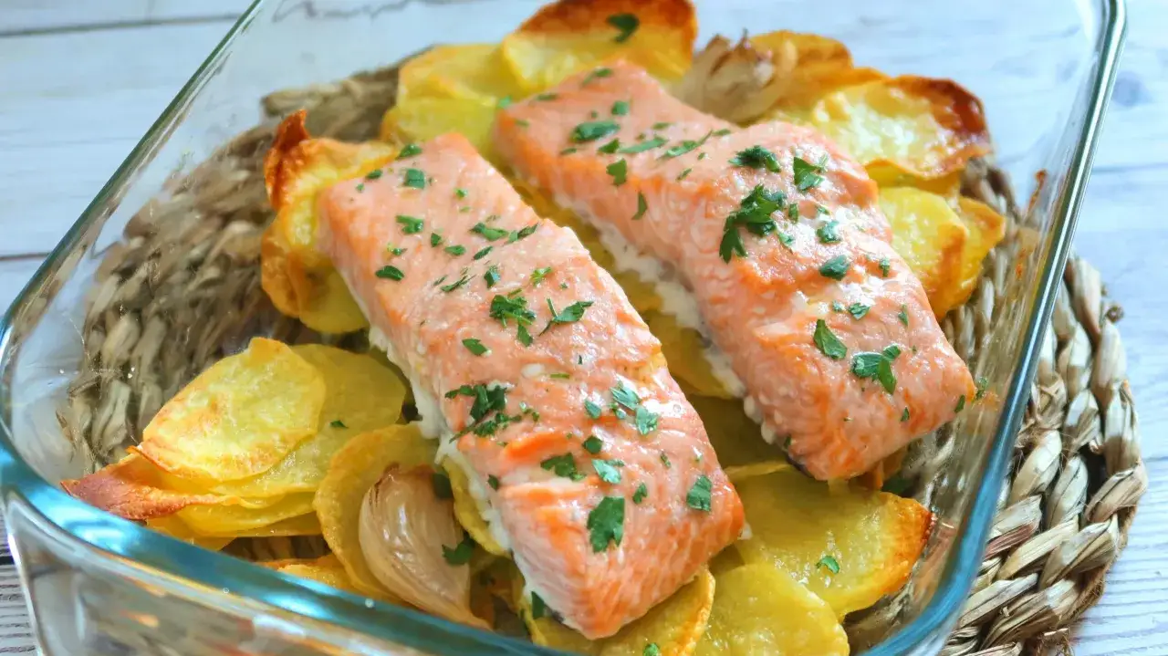 Dos jugosos filetes de salm&oacute;n al horno reposan sobre patatas doradas y ajo asado, todo espolvoreado con perejil fresco.