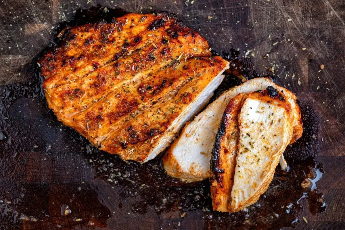 Pechuga de pollo en freidora de aire, dorada y jugosa, cortada en rodajas sobre tabla de madera.