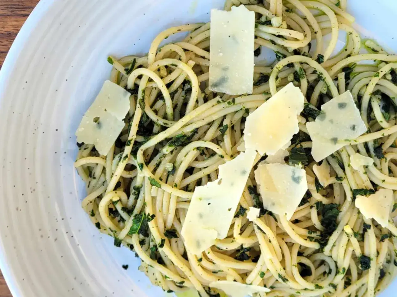 Espaguetis al pesto, un plato vibrante con pasta, hierbas frescas y l&aacute;minas de queso parmesano.