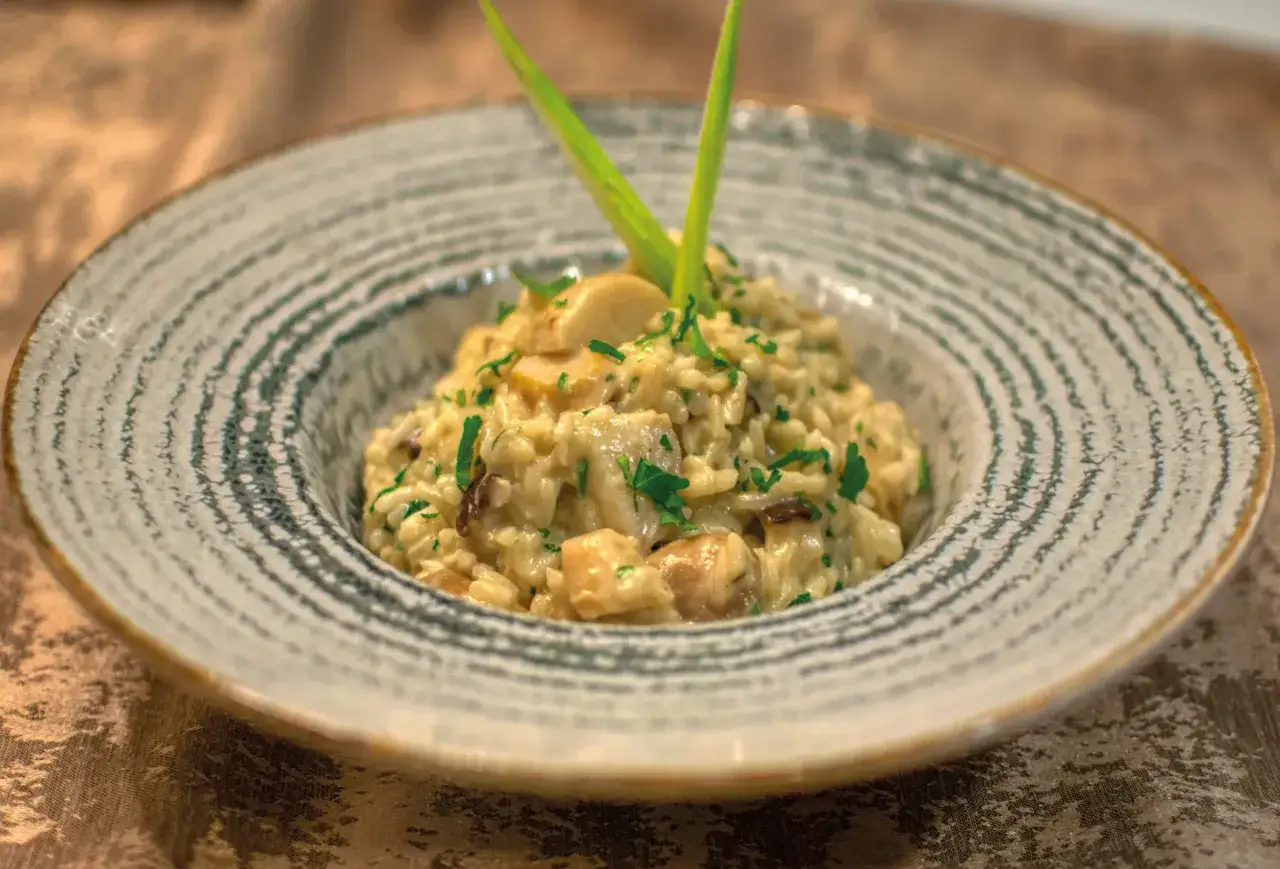 Cremoso risotto de queso con champiñones y perejil fresco, servido en un plato rústico.