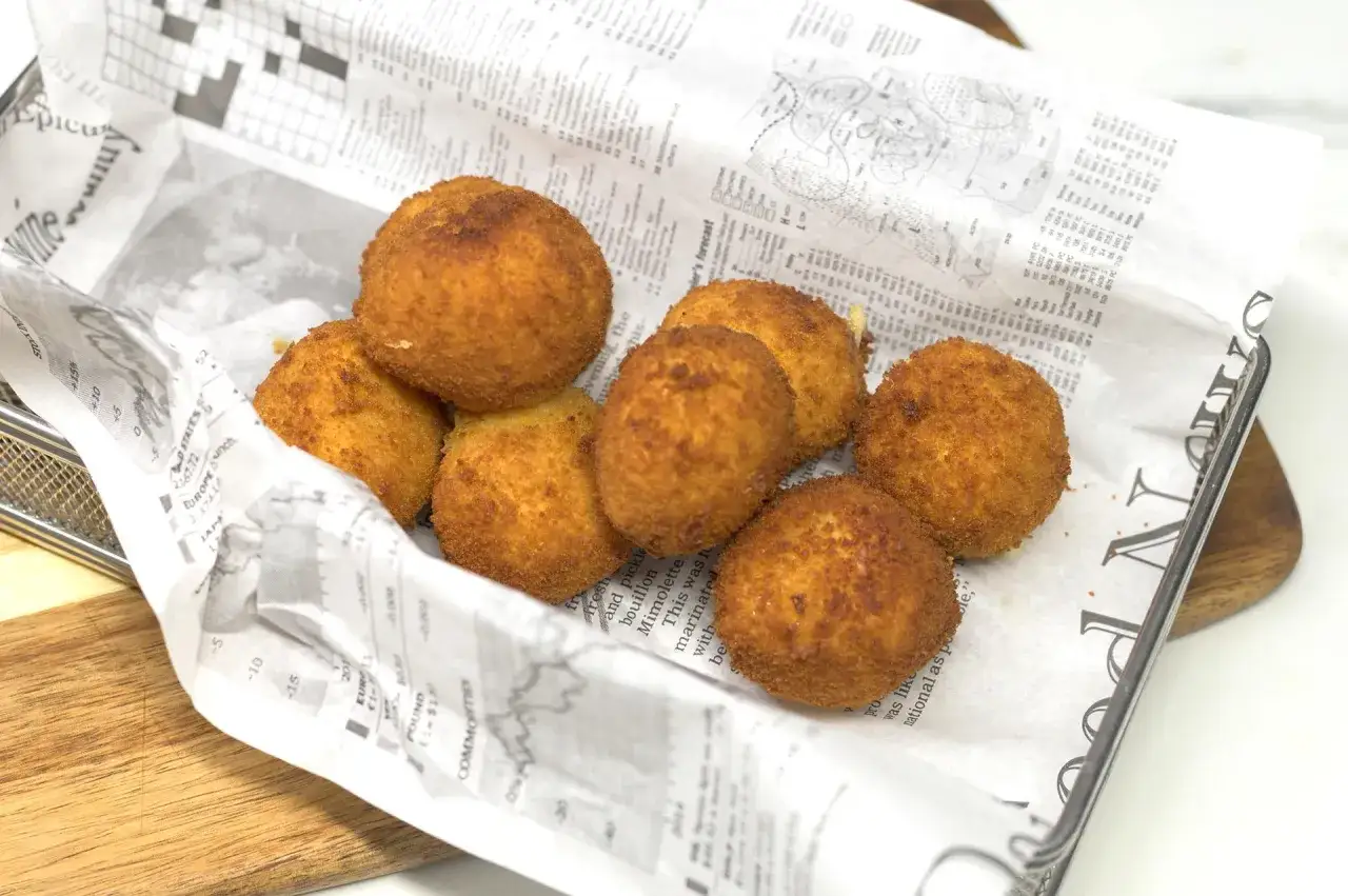 Croquetas de gambas doradas y crujientes, servidas sobre papel de peri&oacute;dico en una cesta met&aacute;lica.