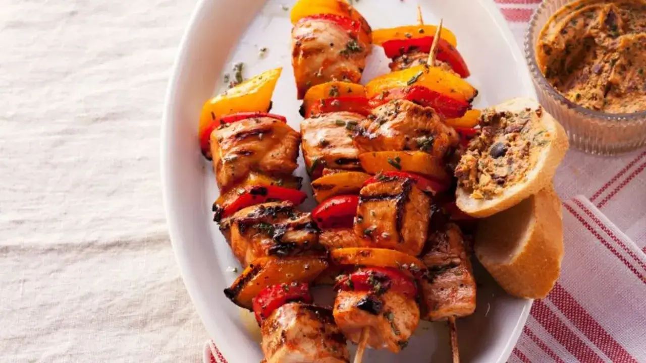 Deliciosos pinchitos de pollo a la parrilla con pimientos rojos y amarillos, servidos con pan y una salsa.