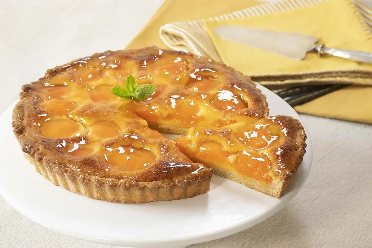 Tarta dorada con trozos de albaricoque y un toque de menta. La mermelada de albaricoque brilla bajo la luz, invitando a probarla.