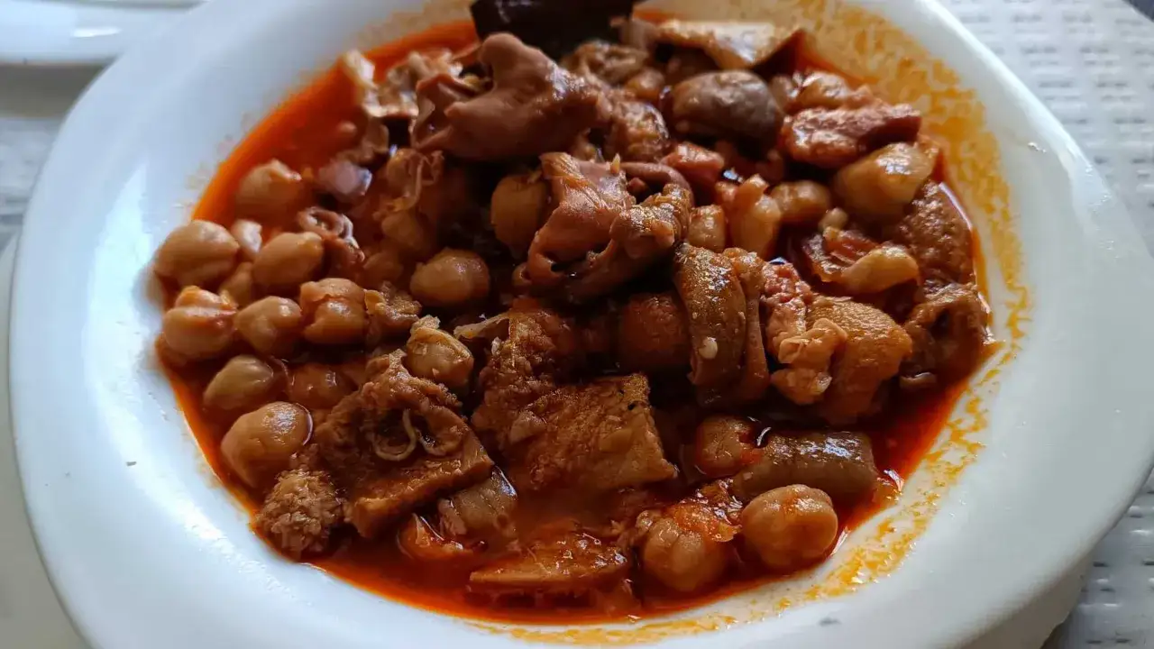 Un plato humeante de callos a la andaluza, con garbanzos tiernos y trozos de carne en una salsa rojiza.