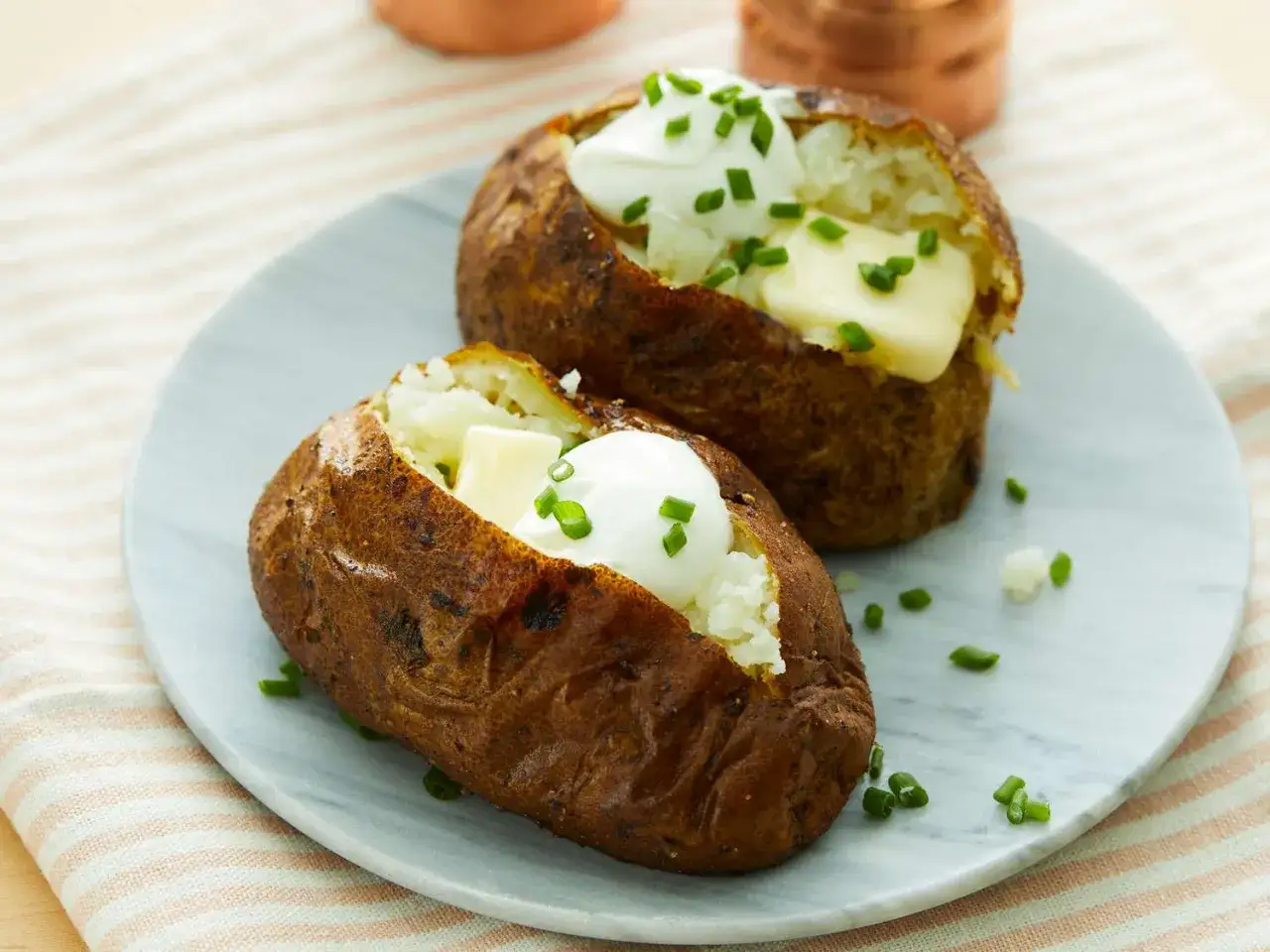 Dos patatas asadas airfryer servidas en un plato, cubiertas con crema agria, mantequilla y cebollino picado.