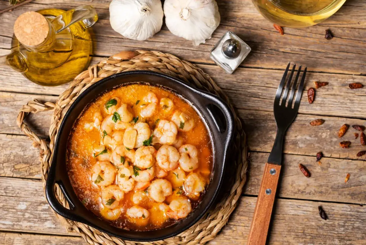 Gambas al pil pil burbujeantes en cazuela de barro, con ajo, guindillas y perejil picado. Aceite de oliva y sal a un lado.