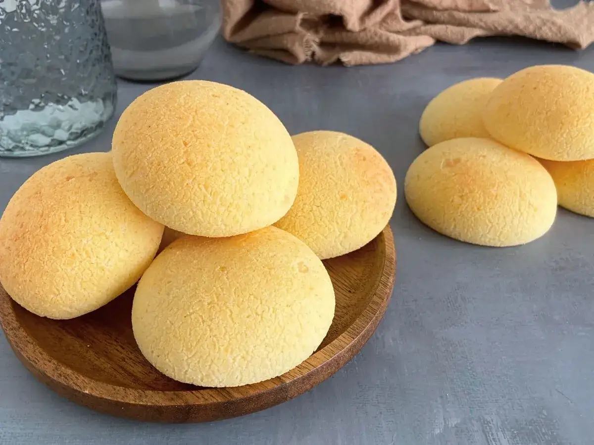 Pan de bono dorados y esponjosos apilados en un plato de madera, listos para disfrutar.