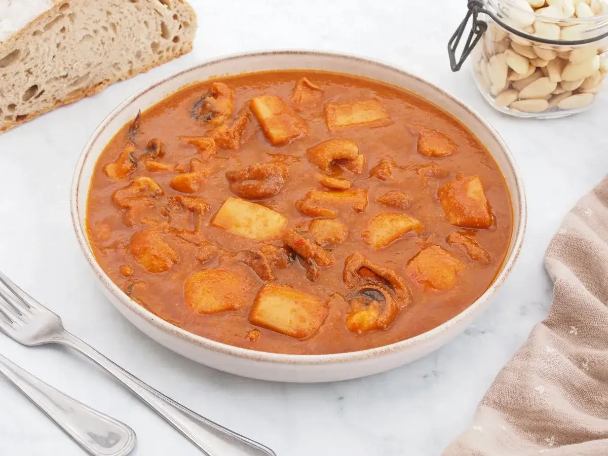 Un plato humeante de jibia en salsa, con trozos de patata y pan r&uacute;stico al lado.