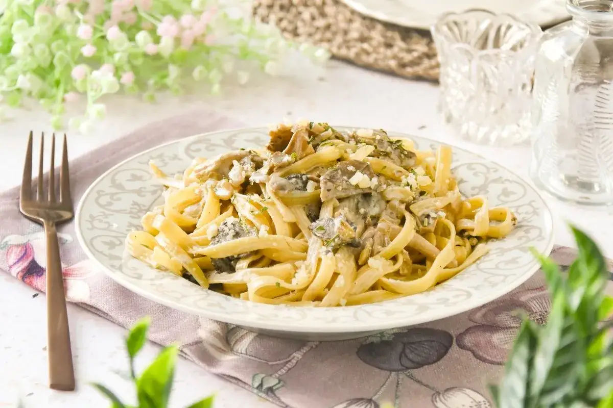 Pasta con setas cremosa, servida en un plato decorado. Un tenedor de bronce descansa a la izquierda.